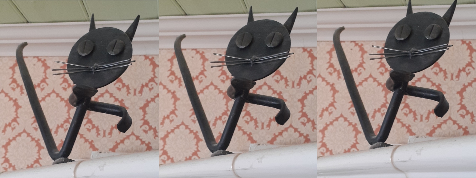 A metal sculpture of a cat, sitting on a pipe in front of some wallpaper. The image is tiled three times.